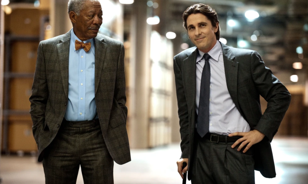 Bruce Wayne está com uma bengala ao lado de Lucius Fox em The Dark Knight Rises.