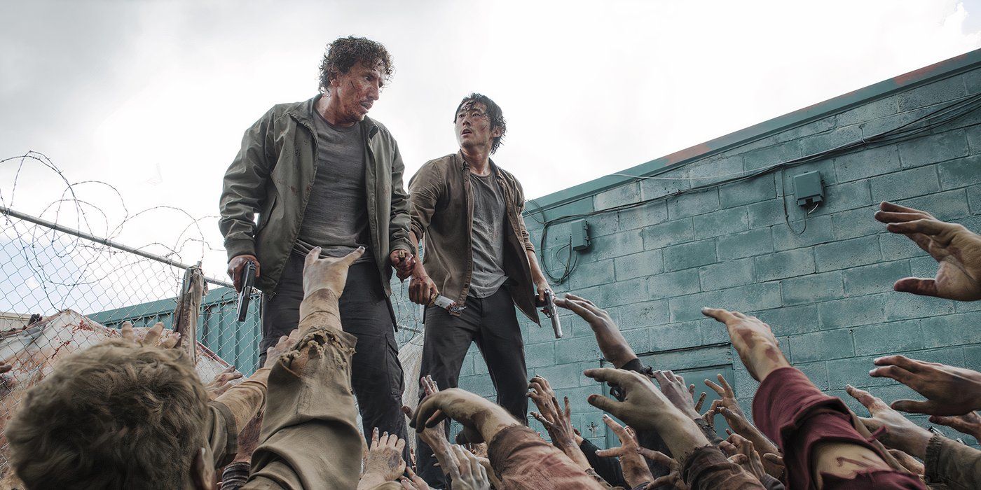 Glenn and Nicholas from The Walking Dead standing atop a dumpster crowded by walkers.