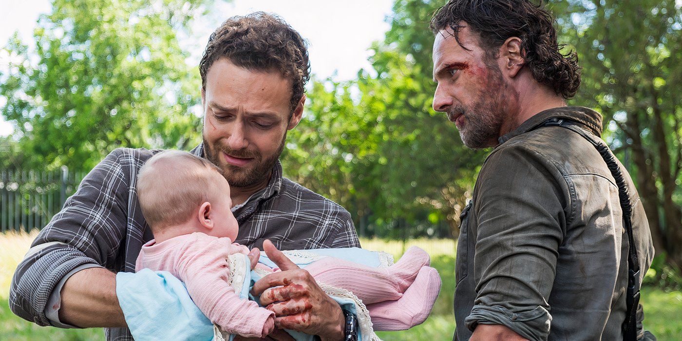 Aaron looking tearful with joy while holding baby Gracie as Rick looks on in The Walking Dead