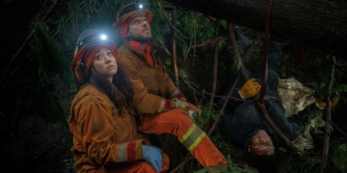 Fiona Rene as Rebecca Lee and Max Thieriot as Bode Leone stand over Jules Latimer as Eve Edwards while she is trapped under a tree on Fire Country