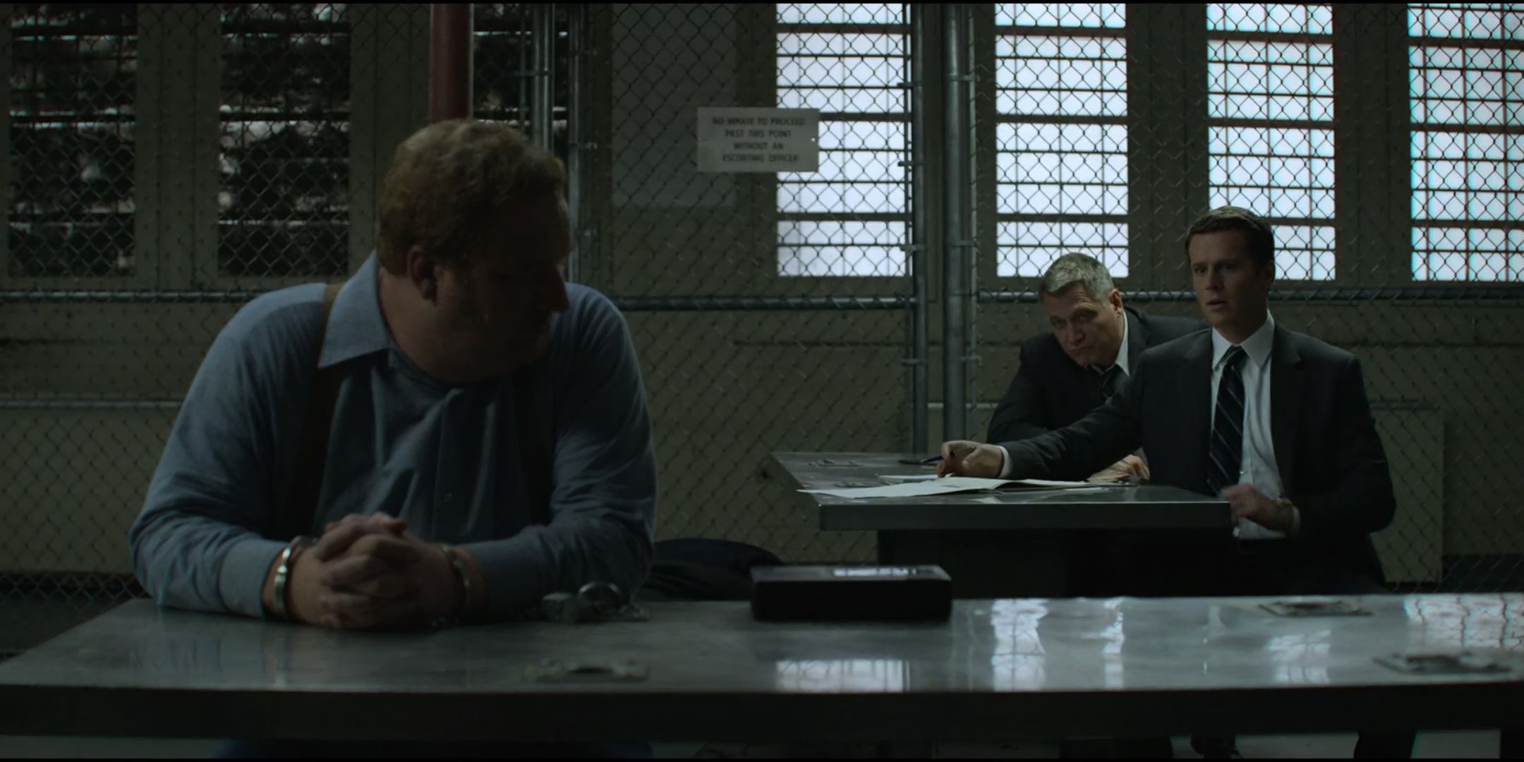 Happy Anderson as Jerry Brudos sits at a table and looks over his shoulder at Jonathan Groff as Holden Ford and Holt McCallany as Bill Tench in Mindhunter