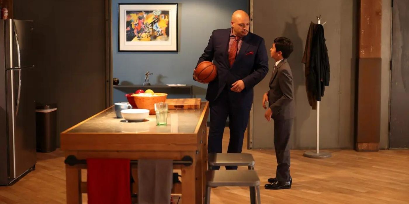 Joe Miñoso as Joe Cruz stands in a kitchen in a blue suit holding a basketball while talking to Carlos S. Sanchez as Javi Cruise in a grey suit on Chicago Fire