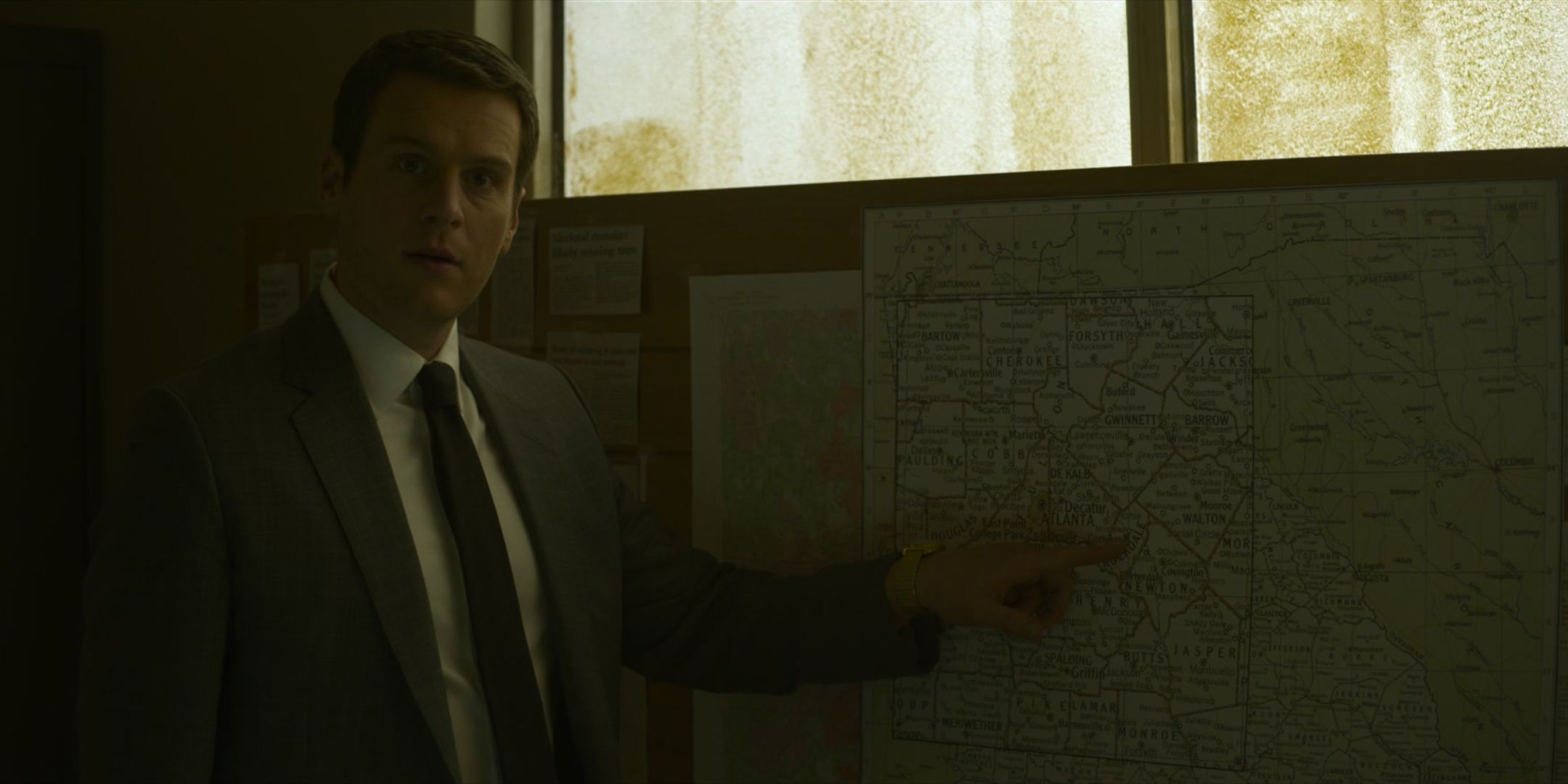 Jonathan Groff as Holden Ford points at a map in a suit in Mindhunter