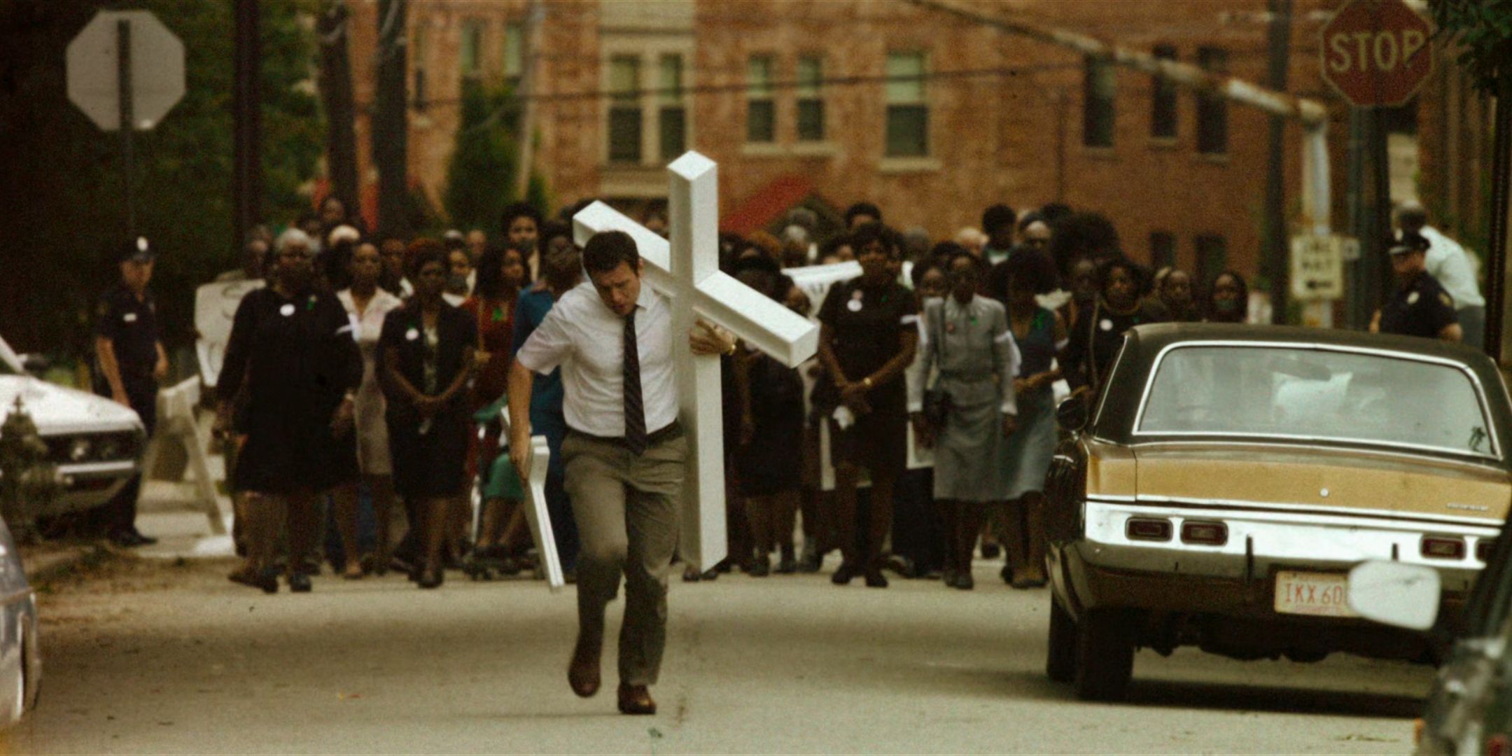 Jonathan Groff as Holden Ford runs with a cross in his arm in front of a crowd of grieving black Atlanta residents in Mindhunter