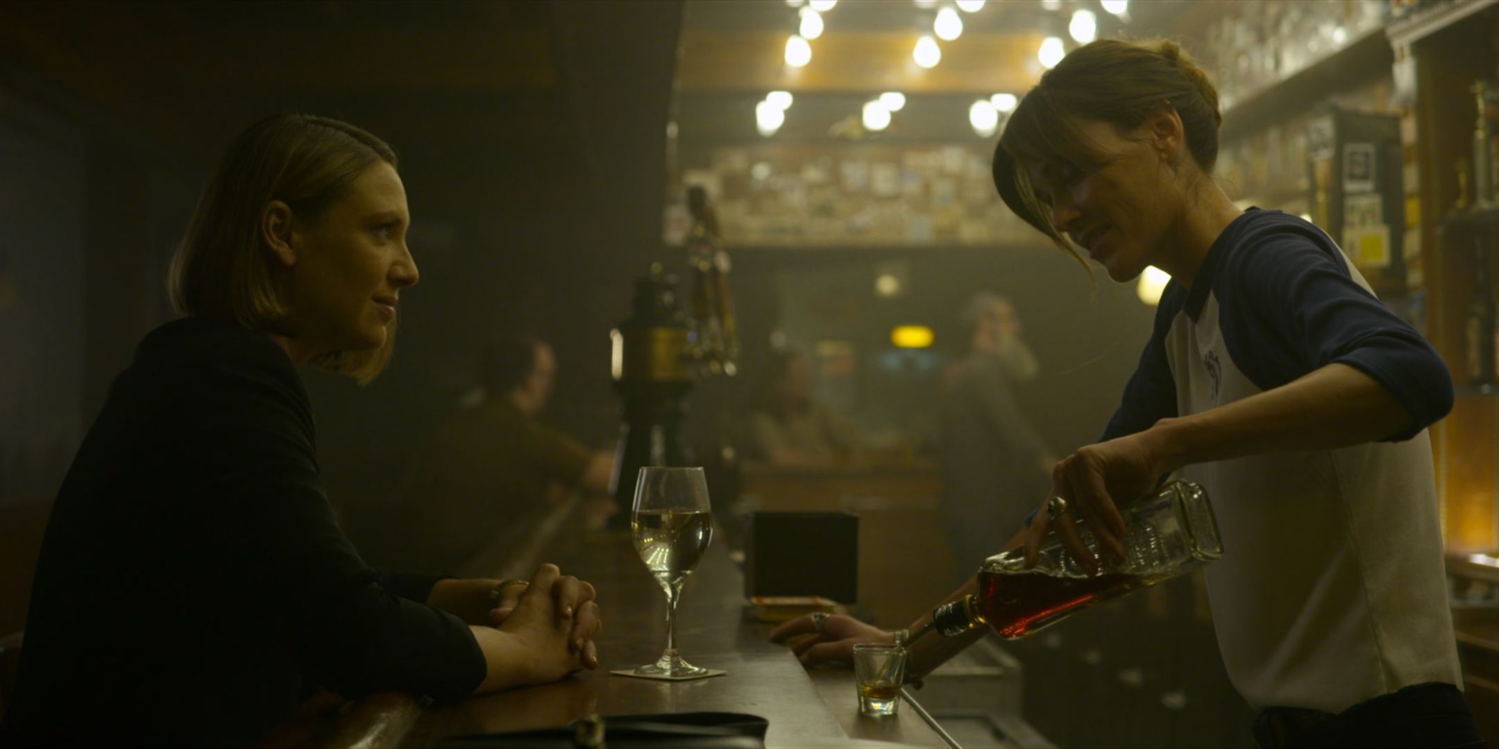 Lauren Glazier as Kay Manz pours a drink for Anna Torv as Wendy Carr at a bar in Mindhunter