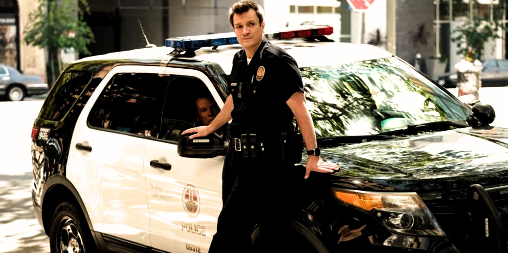 Officer John Nolan (Nathan Fillion) leaning up against his police car in the Rookie