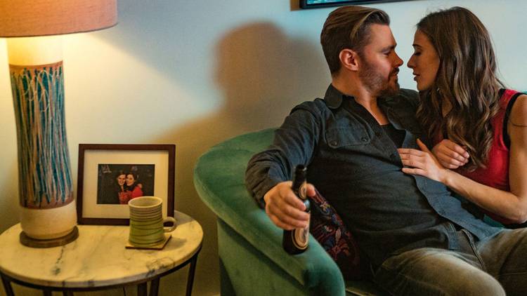 Patrick John Flueger as Adam Ruzek and Marina Squerciati as Kim Burgess kiss on their couch on Chicago PD
