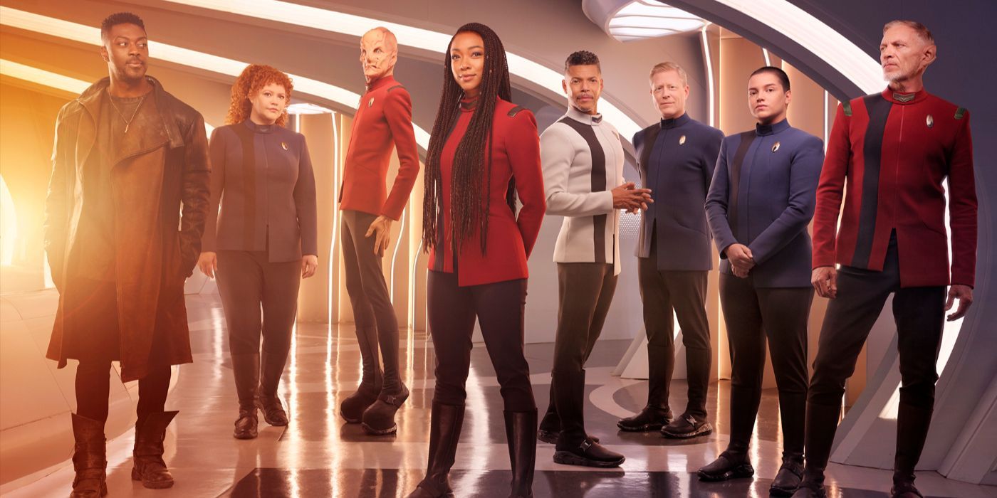 The Star Trek: Discovery Season 5 cast standing in Starfleet uniforms in a starship hallway