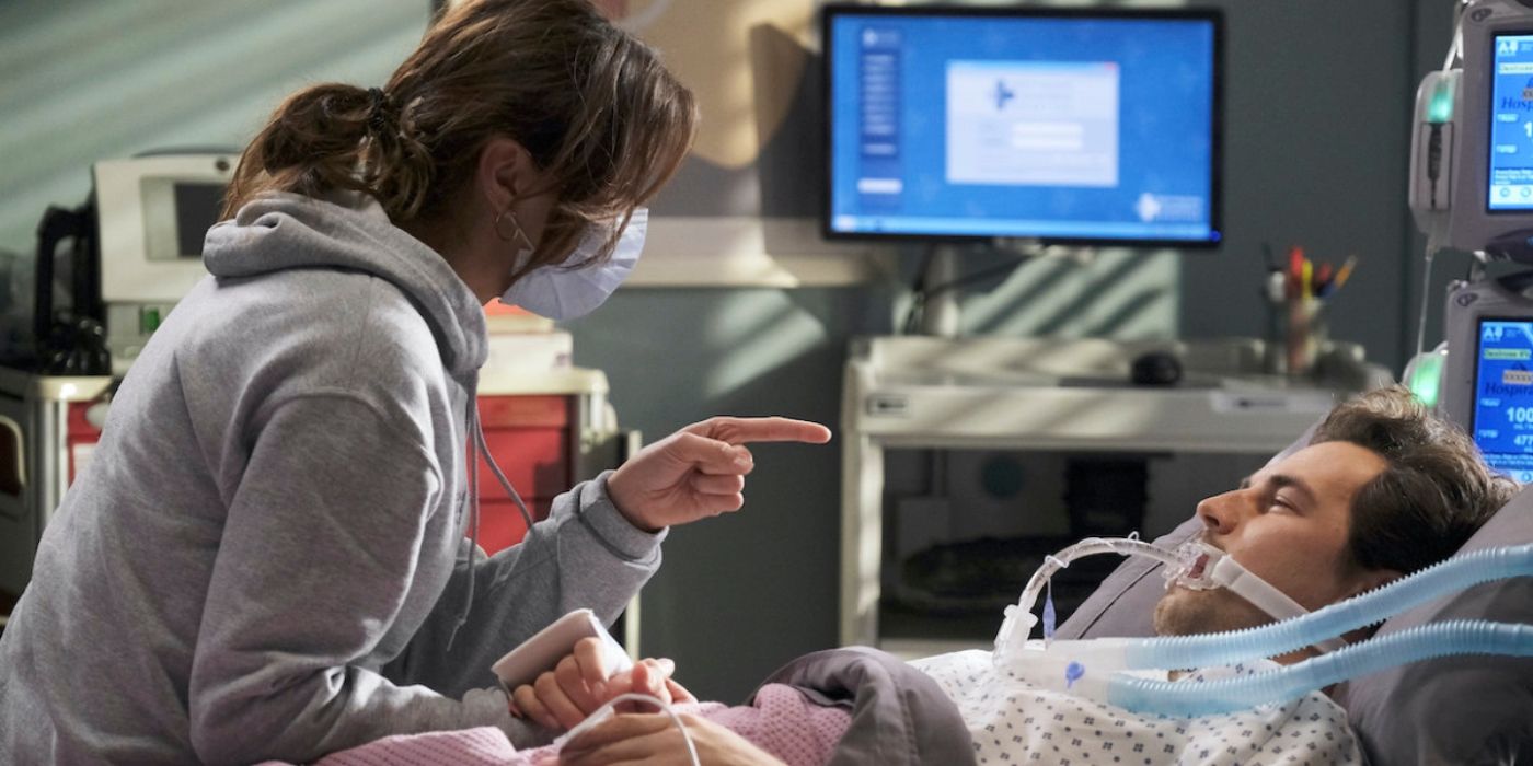 Stefania Spampinato as Carina DeLuca wears a mask and sits at the beside of Giacomo Gianniotti as Andrew DeLuca and tells him to be more careful on Grey's Anatomy