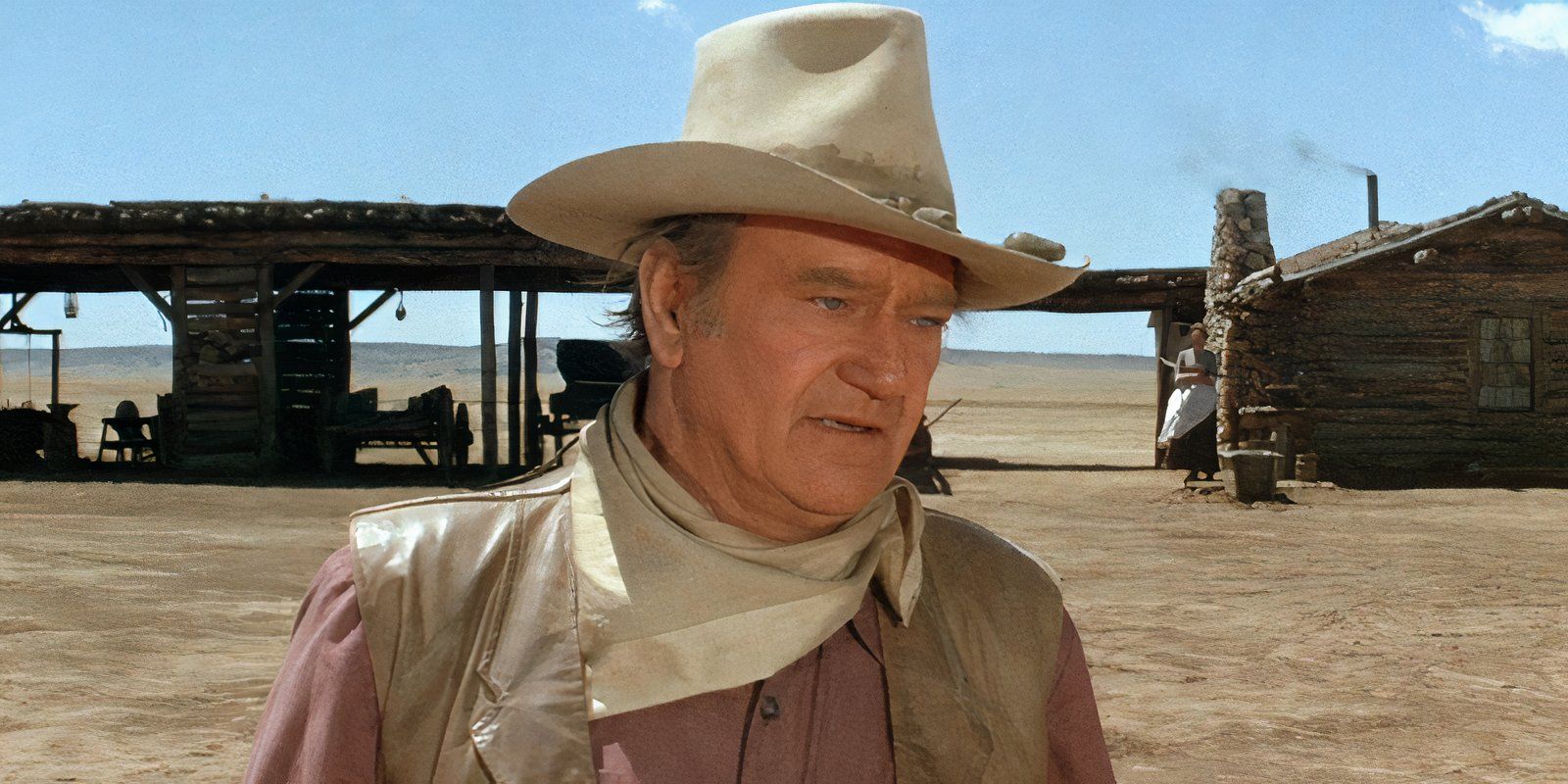 John Wayne stands in a desert landscape.