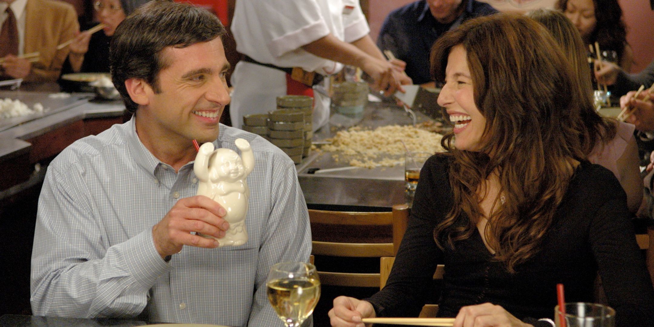 Andy (Steve Carell) y Trish (Catherine Keener) sentados juntos a la mesa y riendo en The 40-Year-Old Virgin