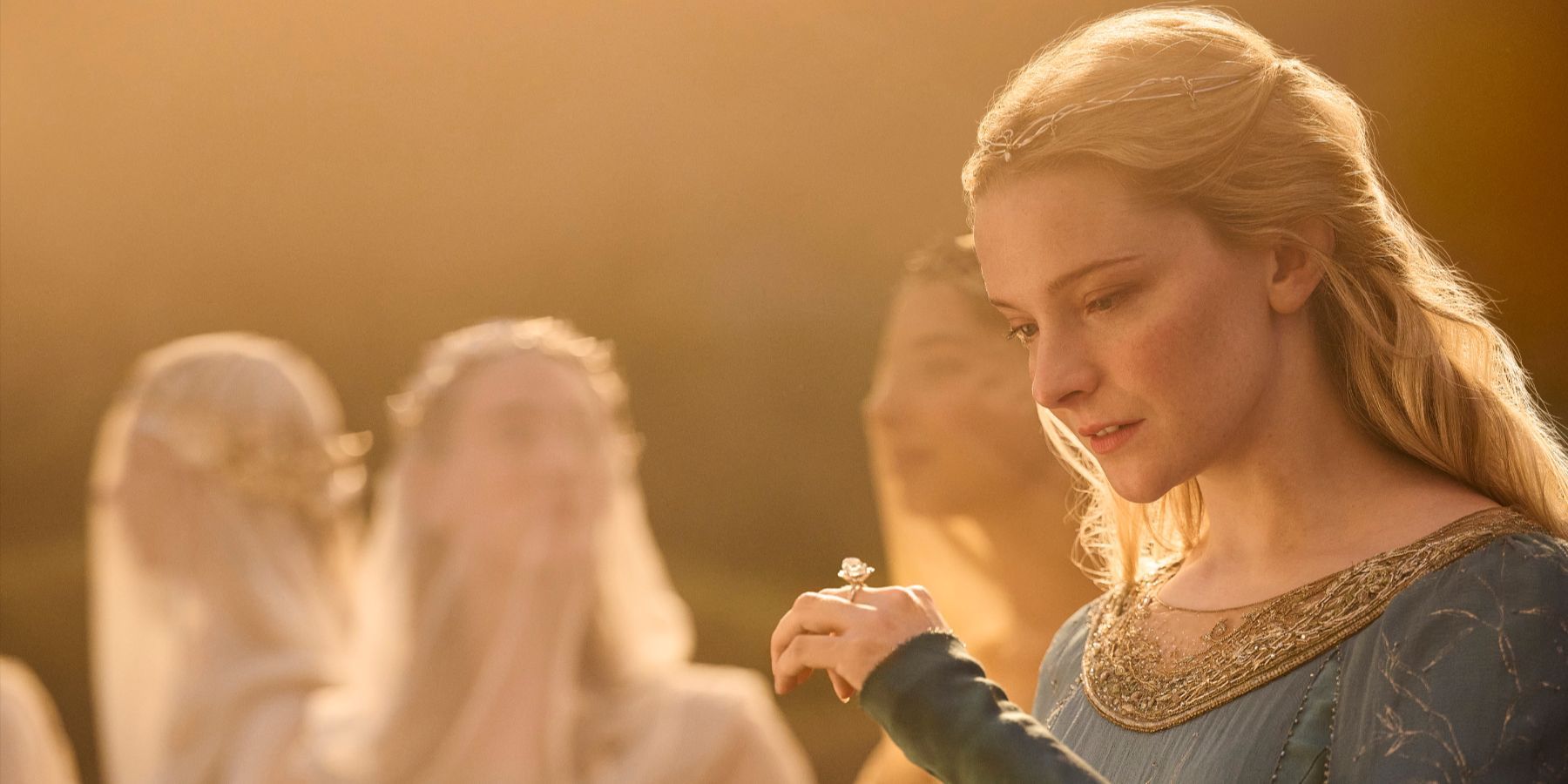 Galadriel, played by Morfydd Clark, in a green dress looking down at her ring in The Rings of Power