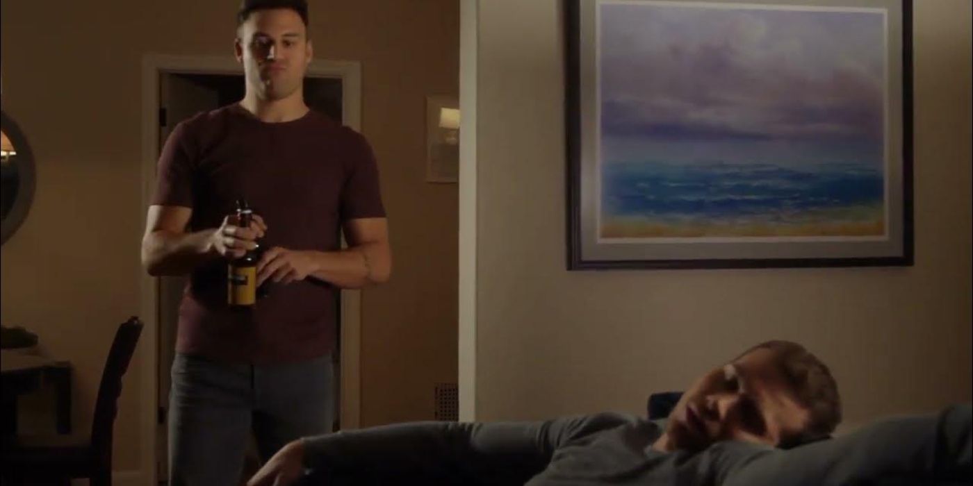 Ryan Guzman as Eddie Diaz holds two beers and watches Oliver Stark as Evan 'Buck' Buckley who is asleep on his couch on 9-1-1