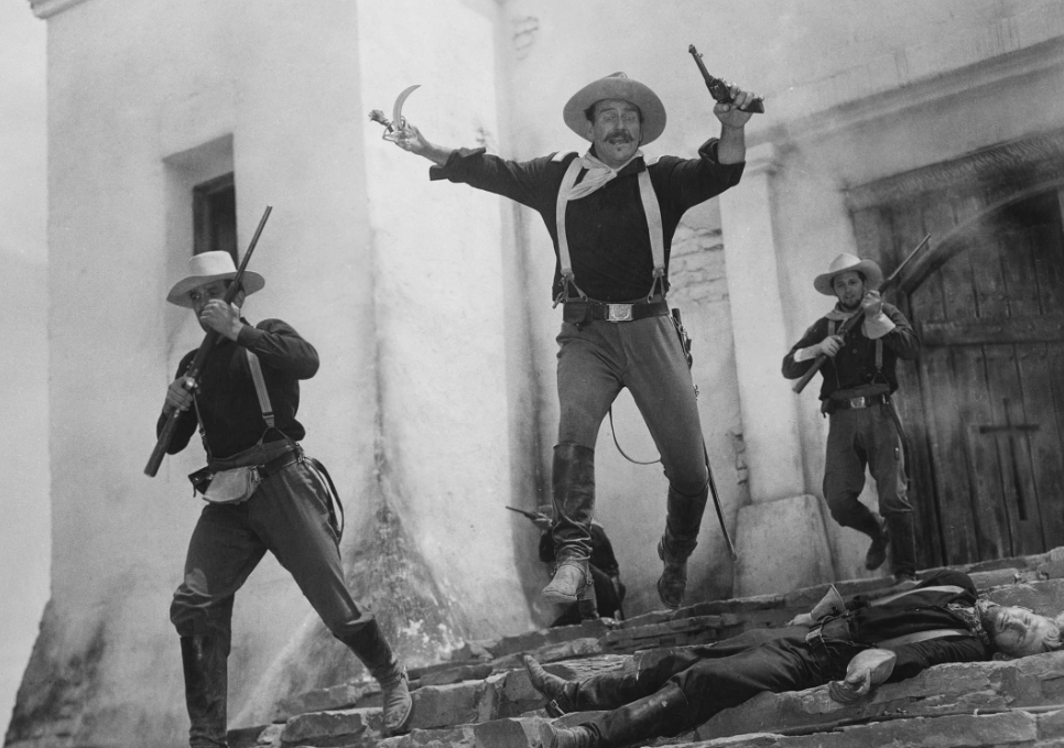 John Wayne sai correndo de um prédio segurando espada e arma e pulando sobre um corpo em Rio Grande.