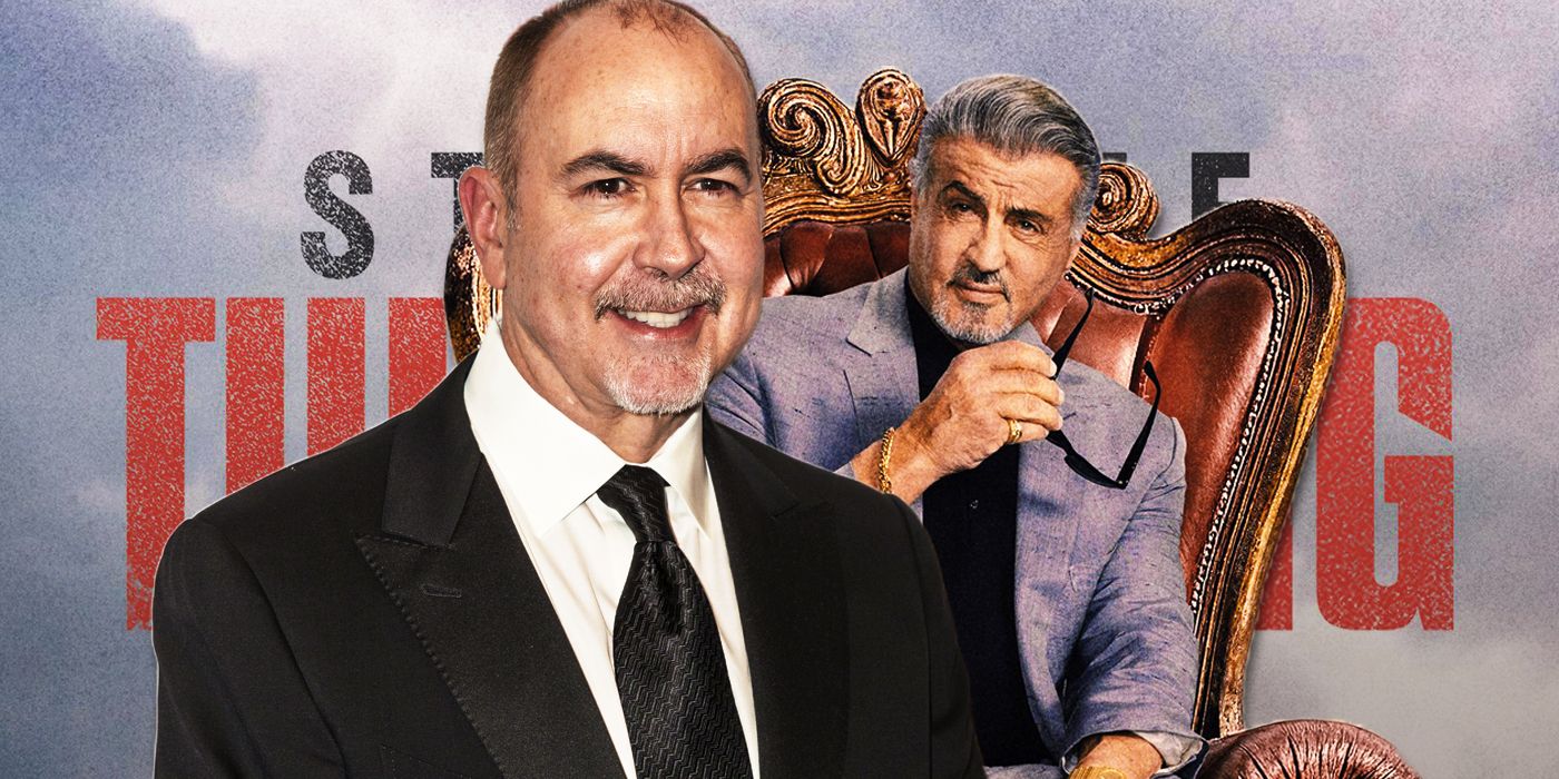 Writer Terence Winter in a black suit in front of Tulsa King poster featuring Sylvester Stallone