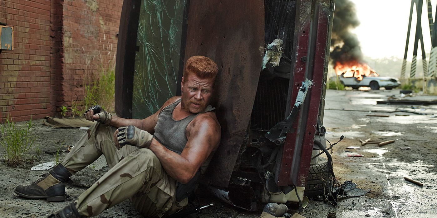 Abraham in a tank top sitting on the ground hiding behind debris in a flashback scene from The Walking Dead.