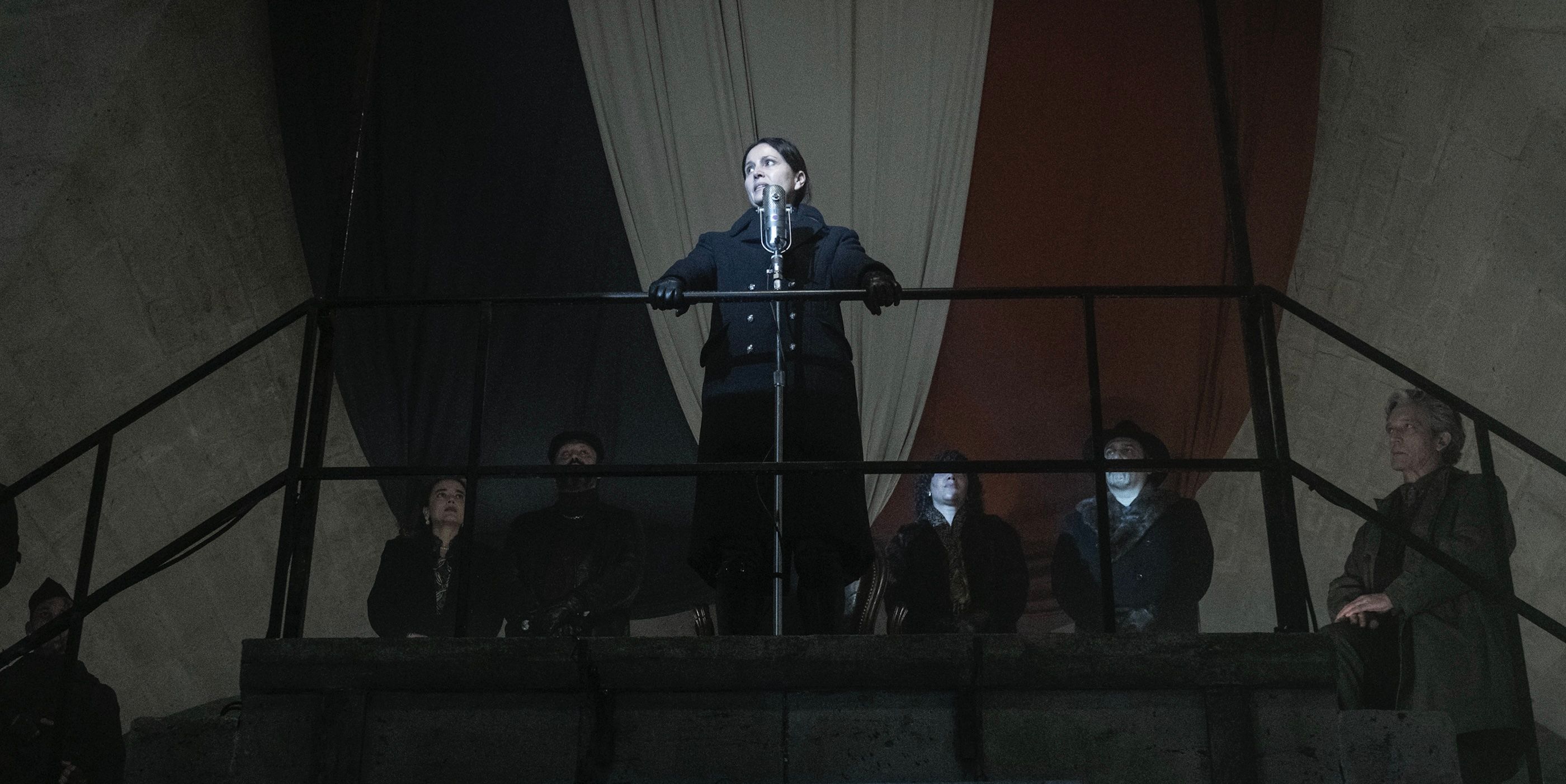 Genet (Anne Charrier) stands on a balcony in front of French flag on The Walking Dead: Daryl Dixon