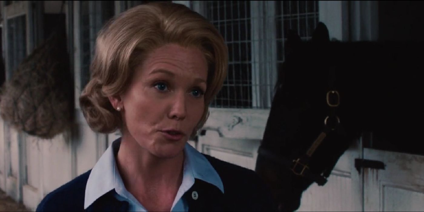 Diane Lane como Penny Chenery conversando com alguém no estábulo da Secretaria