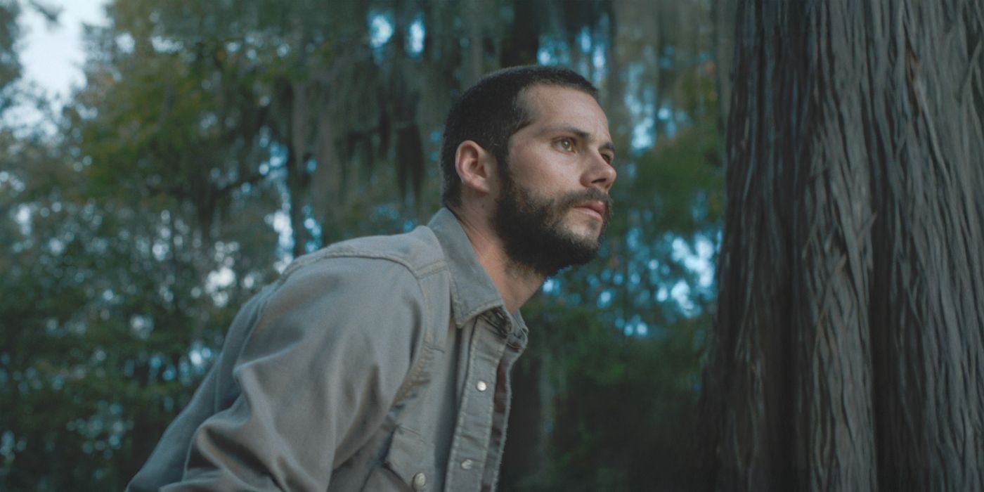 Paris, interpretada por Dylan O'Brien, vestindo uma camisa jeans em uma floresta à noite no filme Caddo Lake