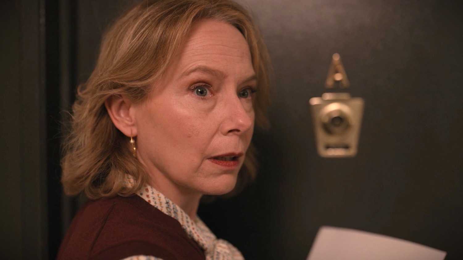 Jan Bellows is standing outside her apartment holding a note in Only Murders in the Building Season 1.