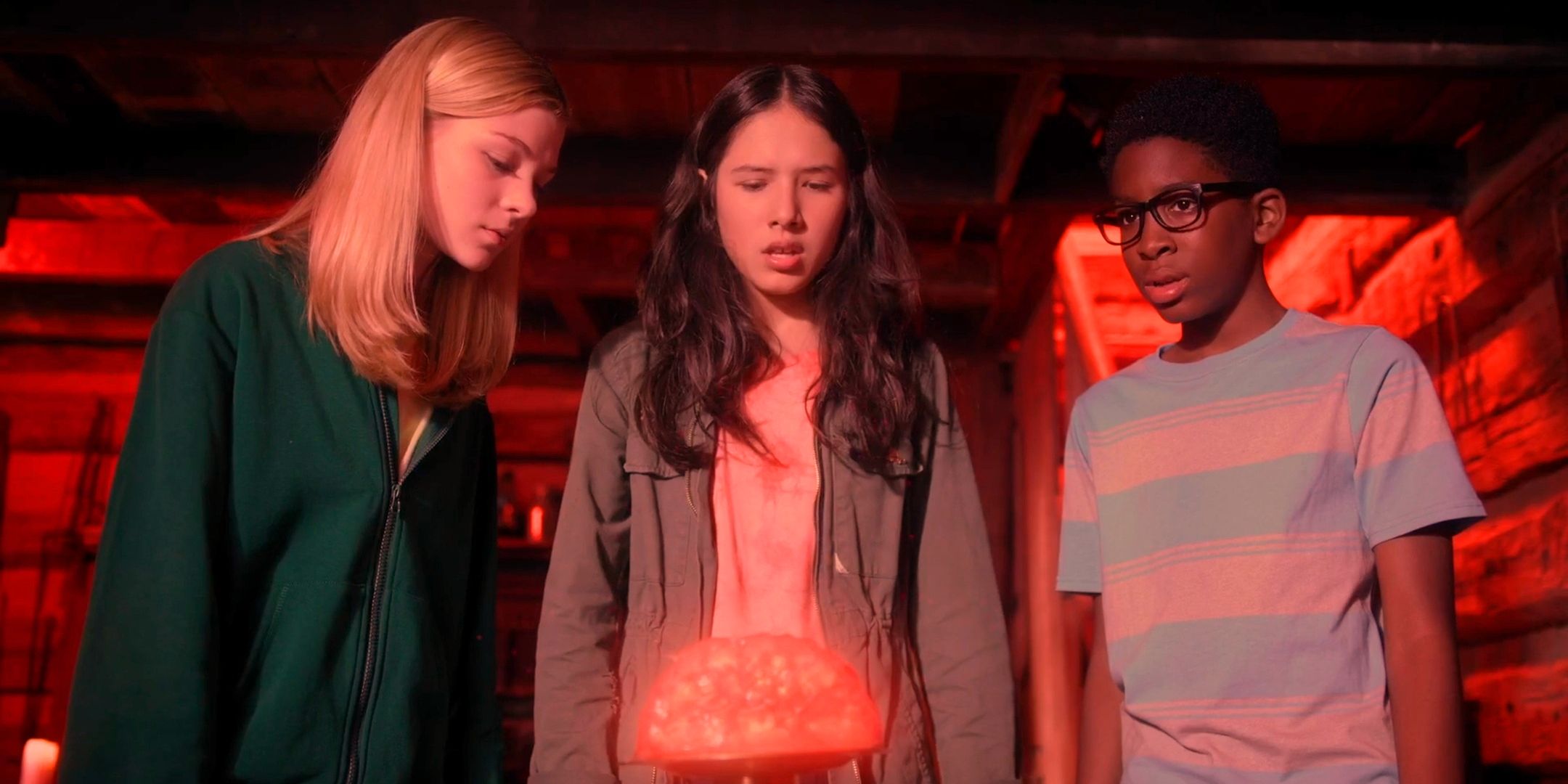 Leah Tessa and Marshy looking worried in a cabin bathed in red light looking at a magical orb from Treasure Trackers