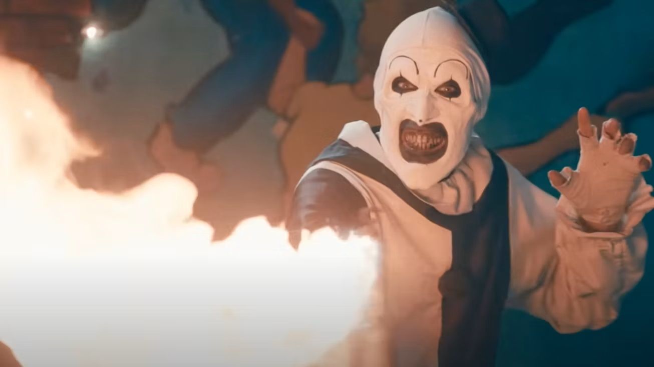 Art the Clown in Terrifier 2 empunhando um pequeno lança-chamas portátil contra o público