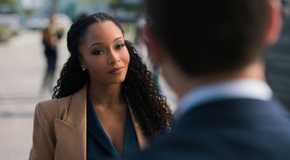 Andrea, played by Yaya DaCosta, stands in front of Mickey in a brown blazer in The Lincoln Lawyer