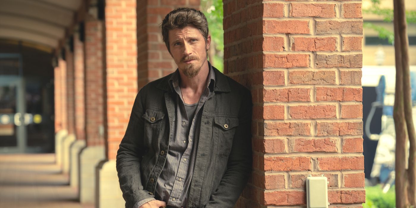 Mitch, interpretado por Garrett Hedlund, encosta-se a uma coluna de tijolos do lado de fora na 2ª temporada de Tulsa King