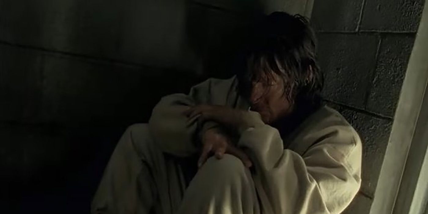 Daryl crouched in a corner in a cell wearing a beige tracksuit in The Walking Dead.