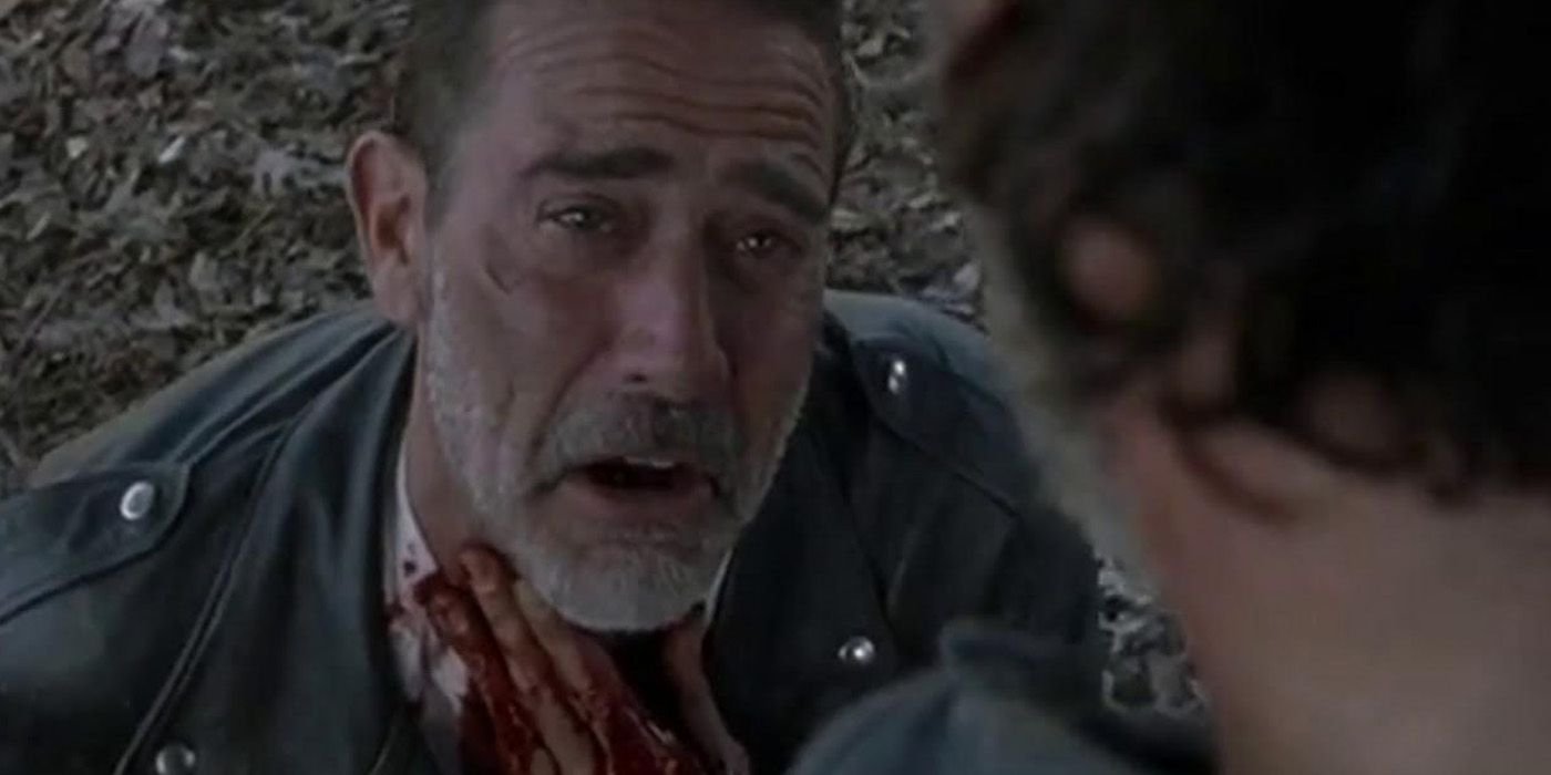 A close-up of Negan holding his bloody neck as Rick looks down on him in The Walking Dead.