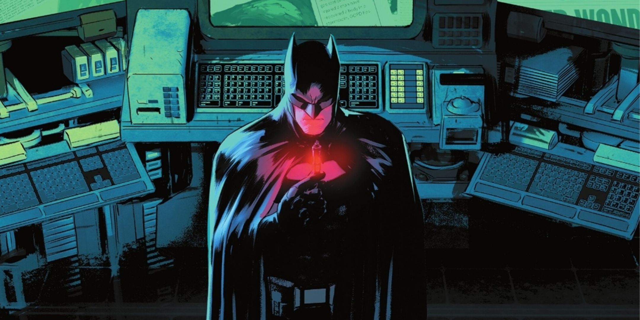 Batman stands over computers in the Batcave.