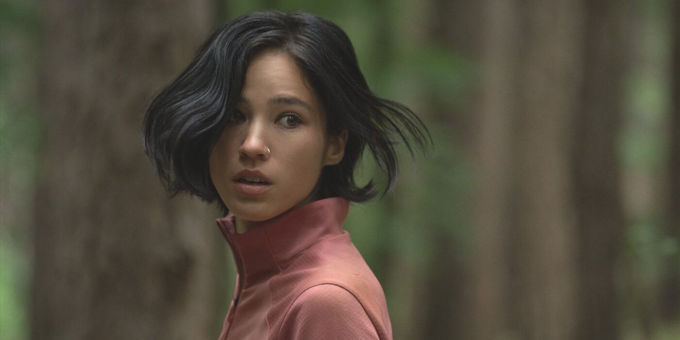 Iris, interpretada por Kelsey Asbille, vestindo uma jaqueta cor de pêssego na floresta no filme da Netflix, Don't Move