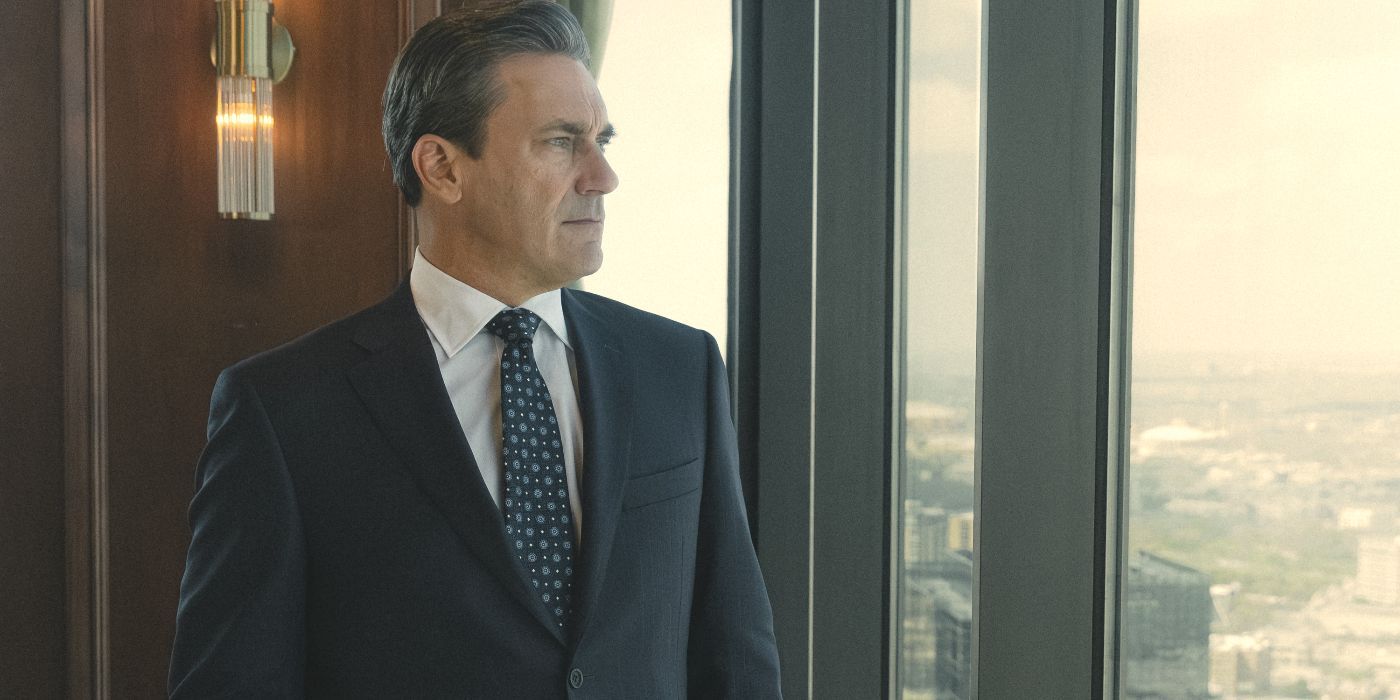 Actor Jon Hamm wearing a black suit and tie, looking out a window in a scene from Landman