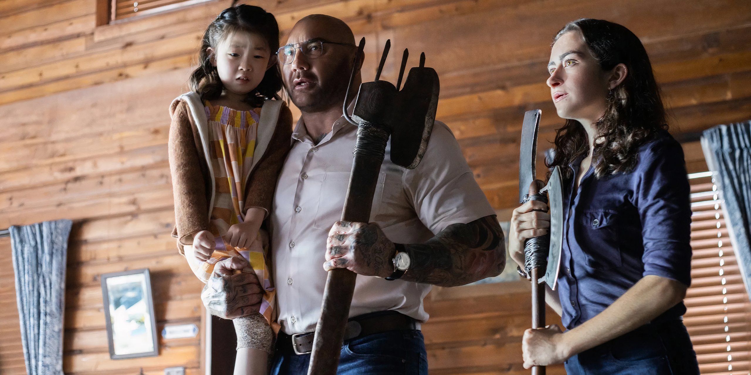 Leonard está segurando Wen e uma arma e ao lado de Adriane em Knock at the Cabin 