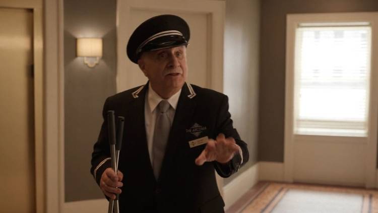 Teddy trying to talk to someone, his hand out, in the lobby of the Arconia on Only Murders in the Building.