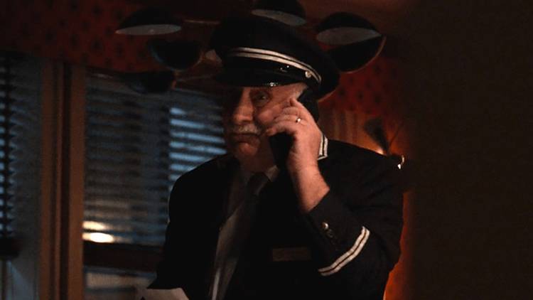 Lester from Only Murders in the Building in an apartment on the phone in the dark.