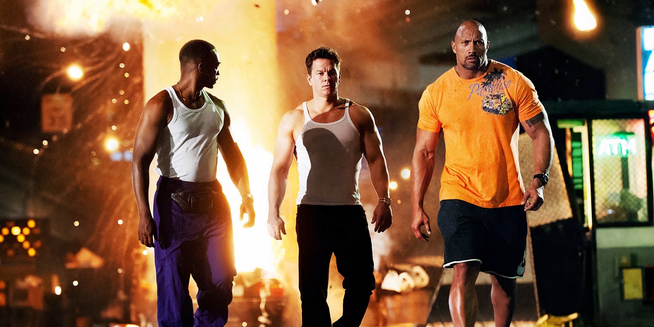 Anthony Mackie, Mark Wahlberg y Dwayne Johnson alejándose de una explosión nocturna en Pain & Gain.