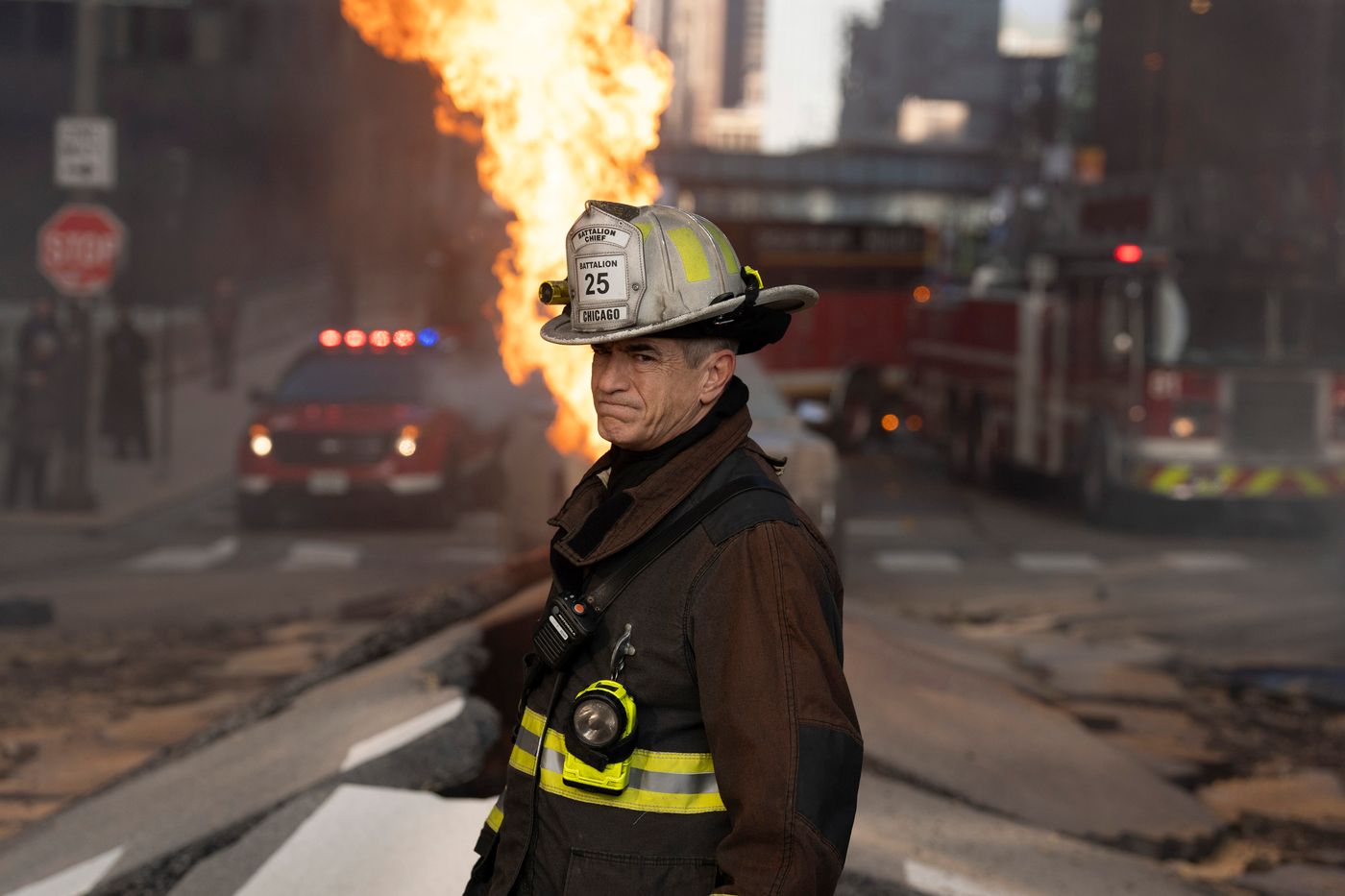 Chief Dom Pascal, wearing firefighter gear, stands in middle of a devastated street on Chicago Fire