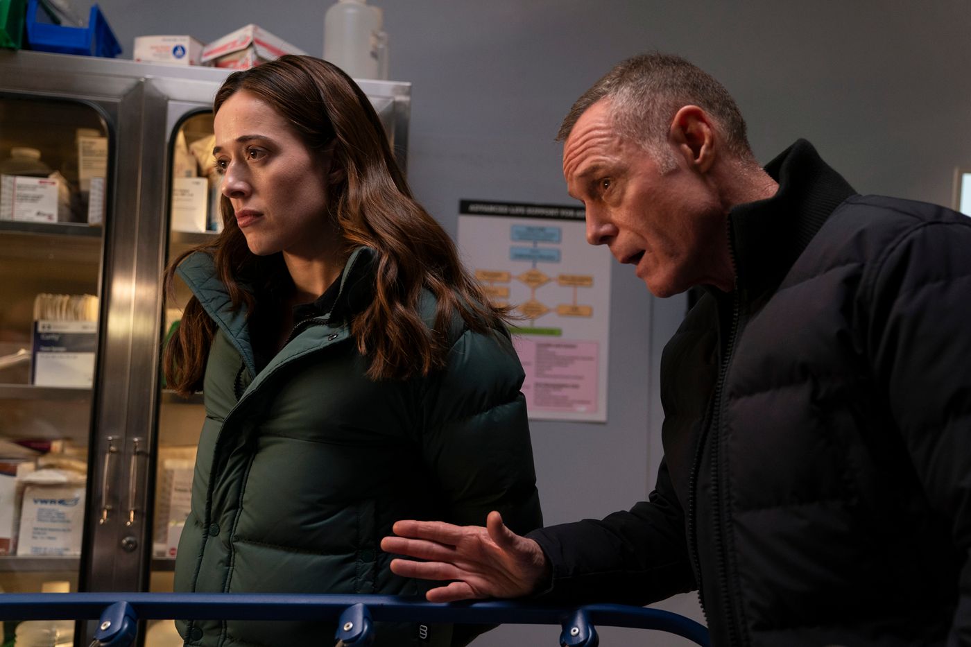 Kim Burgess and Hank Voight stand by a hospital bed at Chicago Med on Chicago Fire