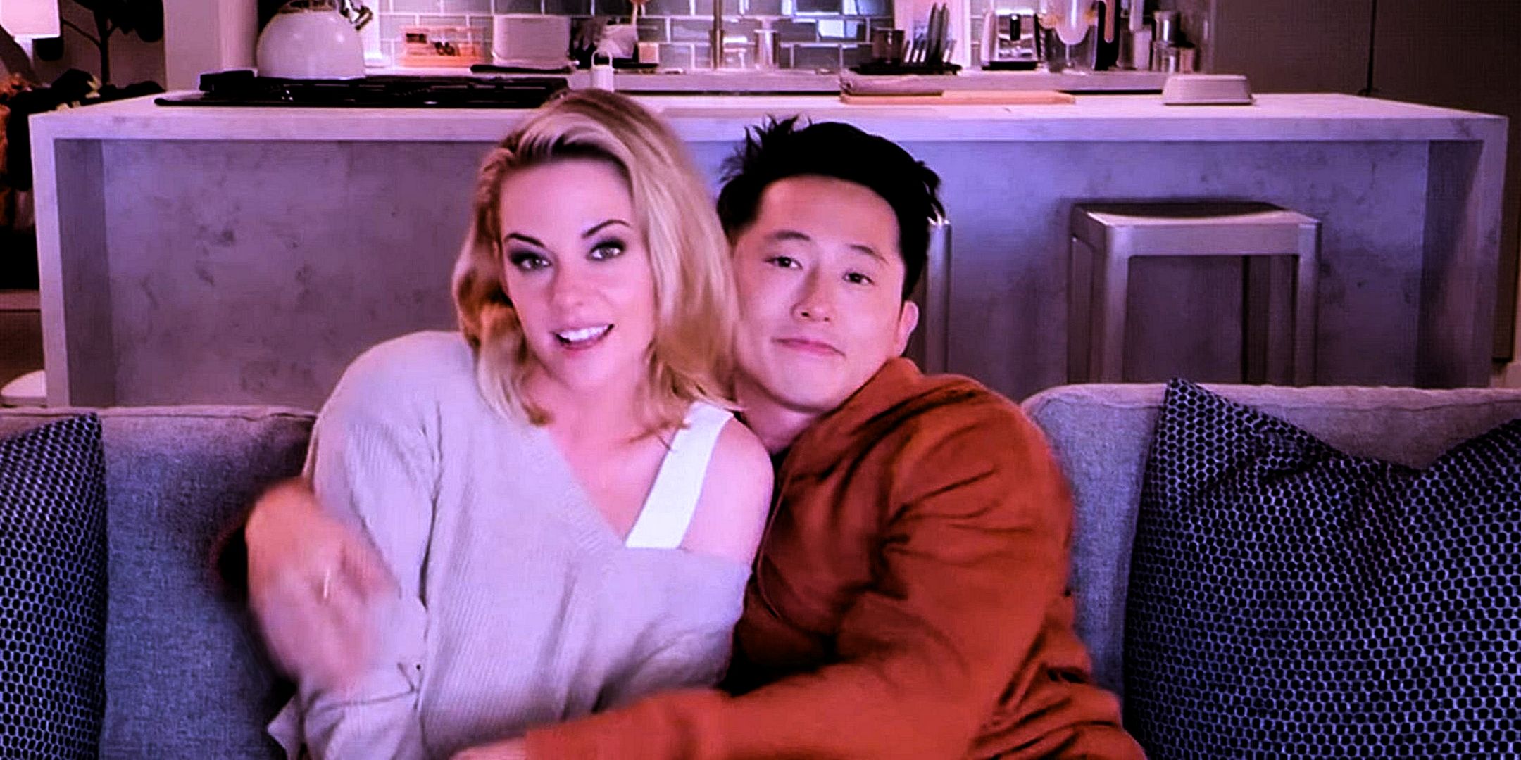 Kristen Stewart as Deja and STeven Yeun as Liam sitting on a couch from Love me