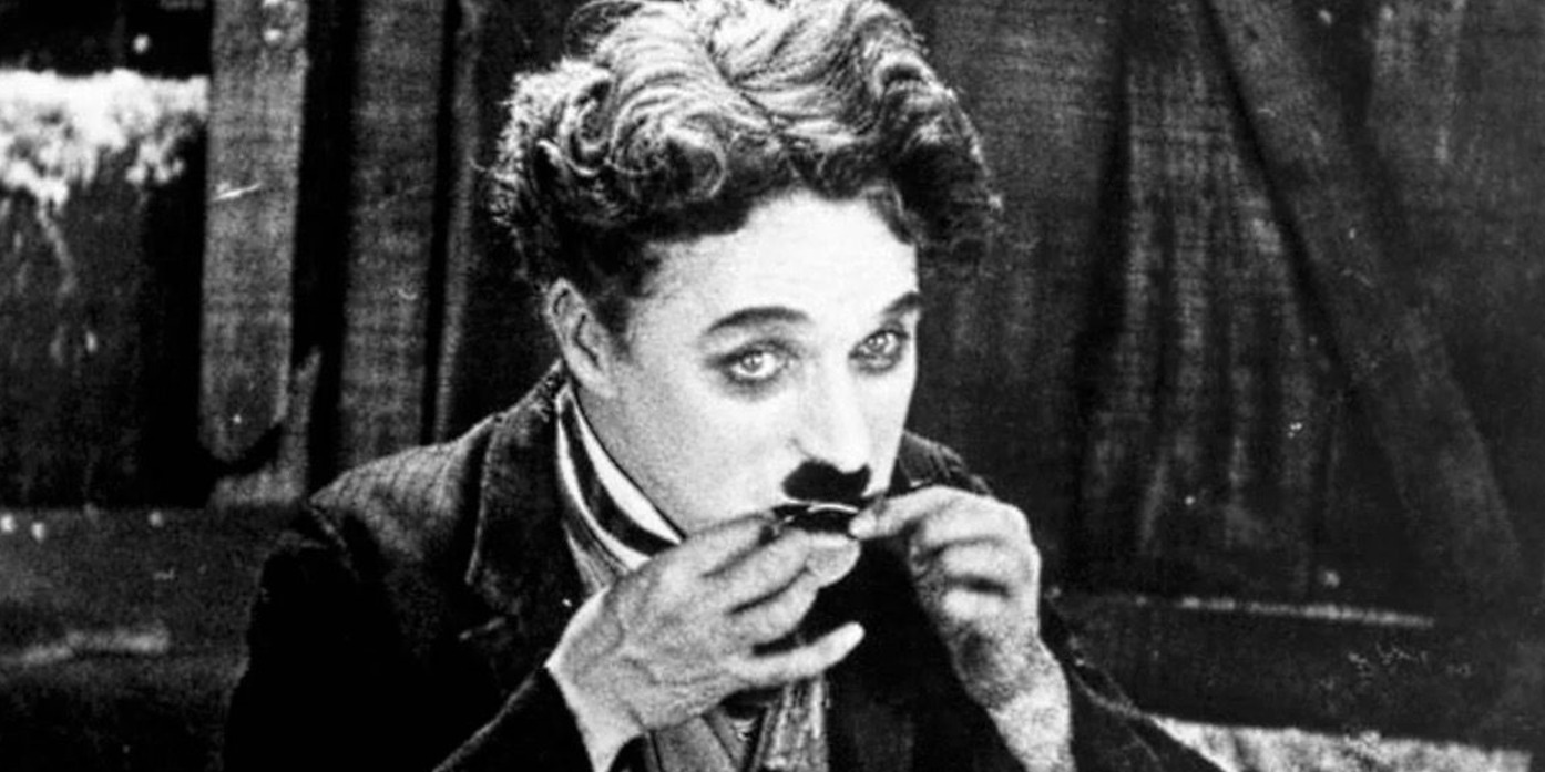 Charlie Chaplin segura algo na boca em The Gold Rush.