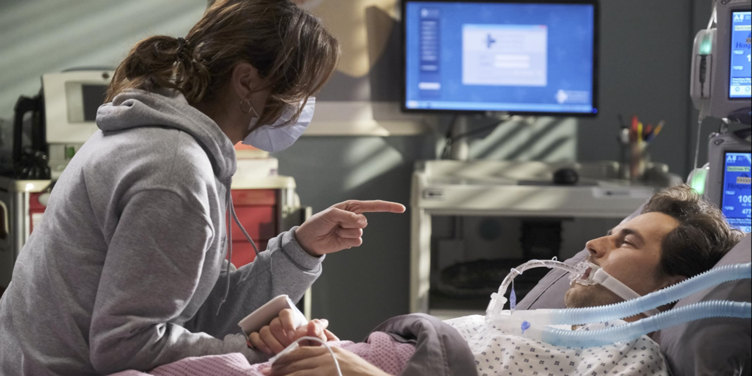 Uma enfermeira segura a mão de Andrew (Giacomo Gianniotti) em uma cama de hospital em Grey's Anatomy.