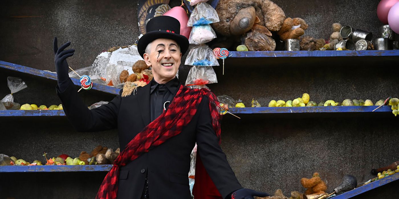 Alan Cumming presenting flamboyantly in a black outfit with top hat and tartan sash in The Traitors.