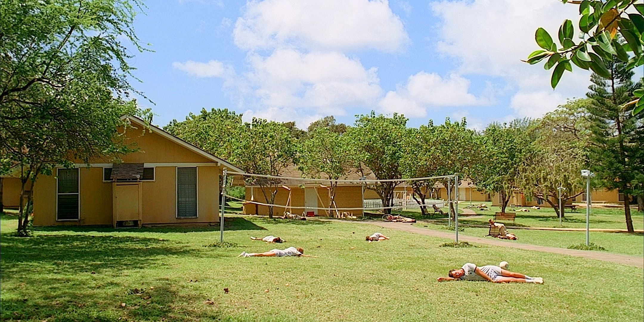 As casas e pátios amarelos do quartel Dharma com cadáveres caídos na grama da série Lost