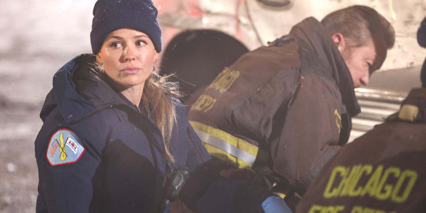 Lizzie Novak wearing blue paramedic jacket, with firefighters working next to her in Chicago Fire