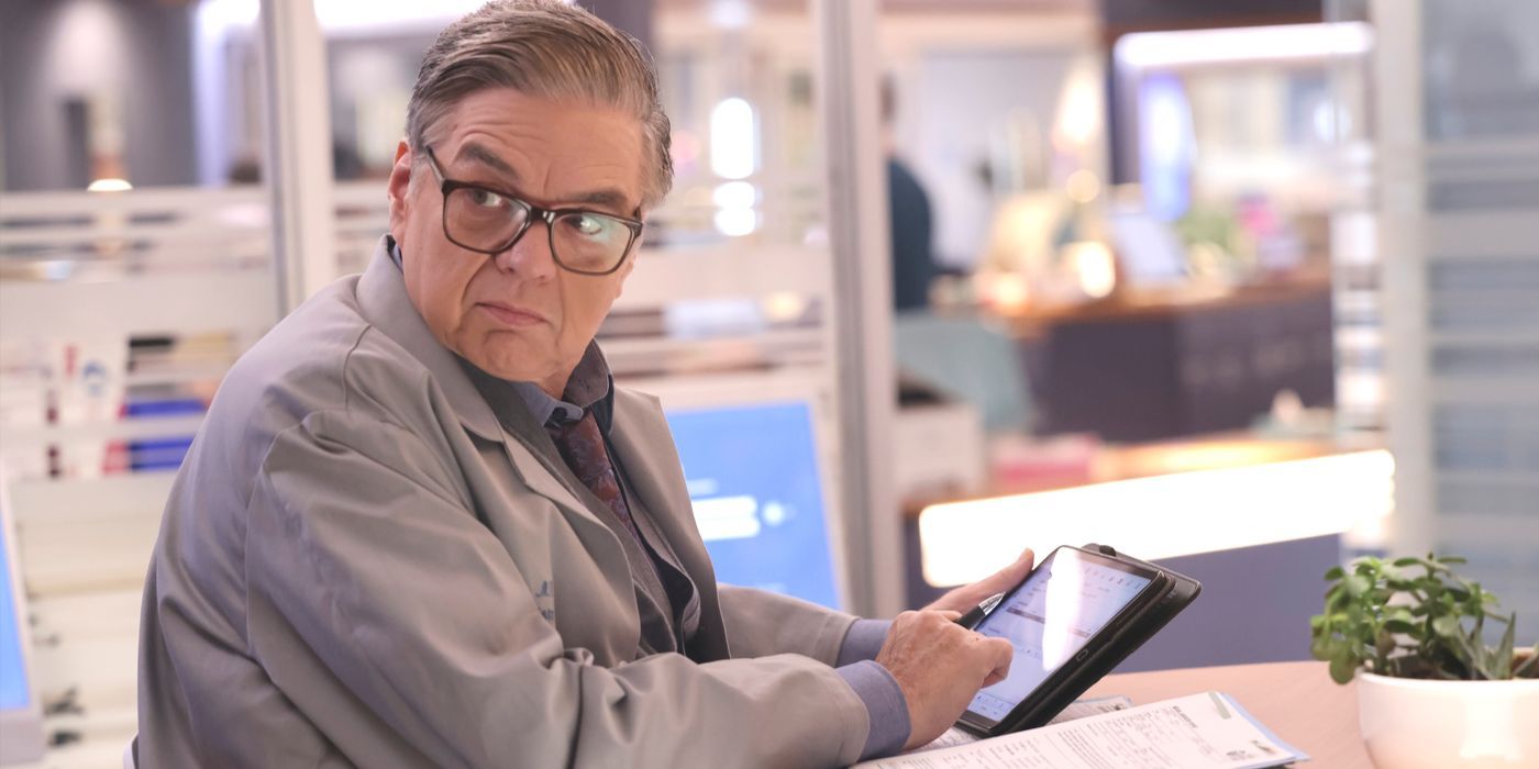 Dr. Daniel Charles, played by Oliver Platt, sits at a work table wearing a lab coat on Chicago Med