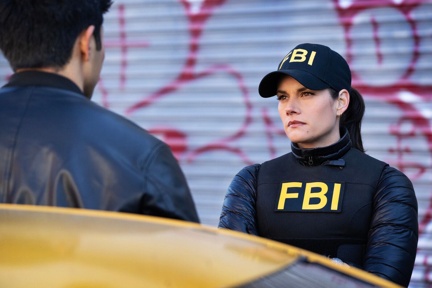 Maggie Bell (Missy Peregrym), wearing a black FBI vest and cap, stands facing a suspect in FBI