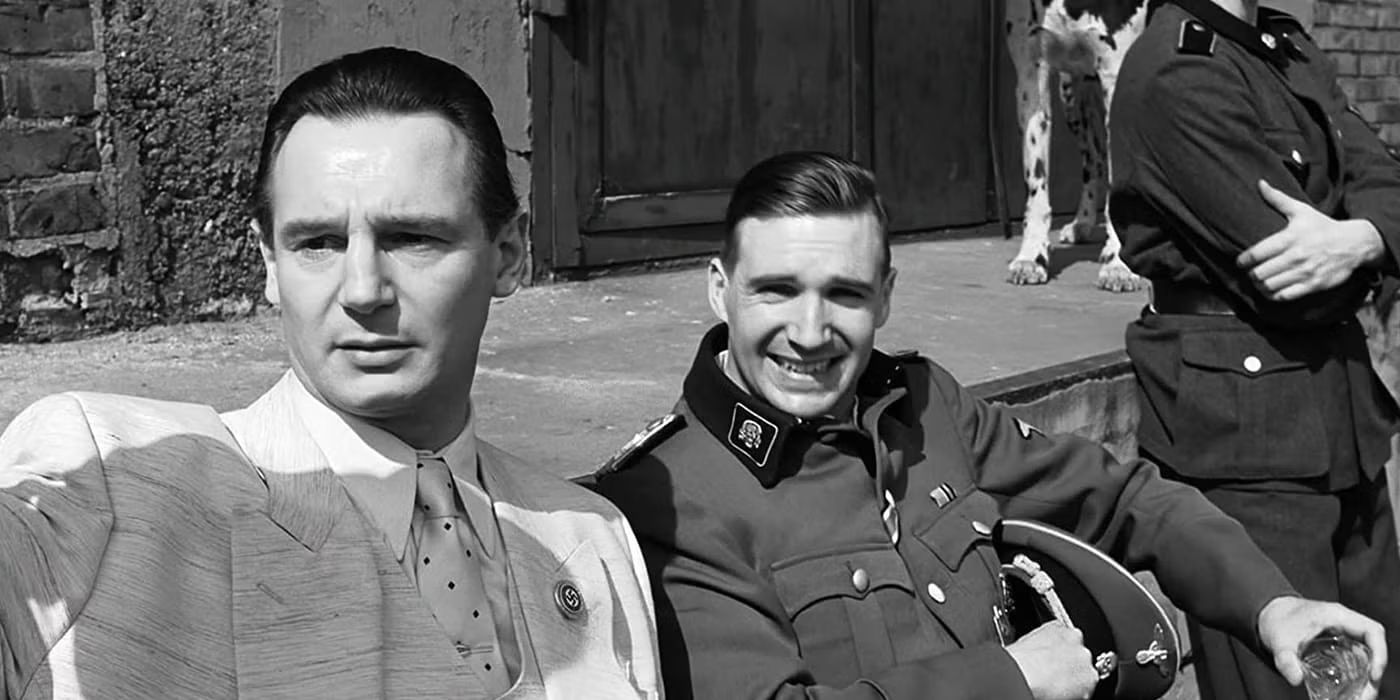 Liam Neeson & Ralph Fiennes look toward the camera while sitting down in Schindler's List