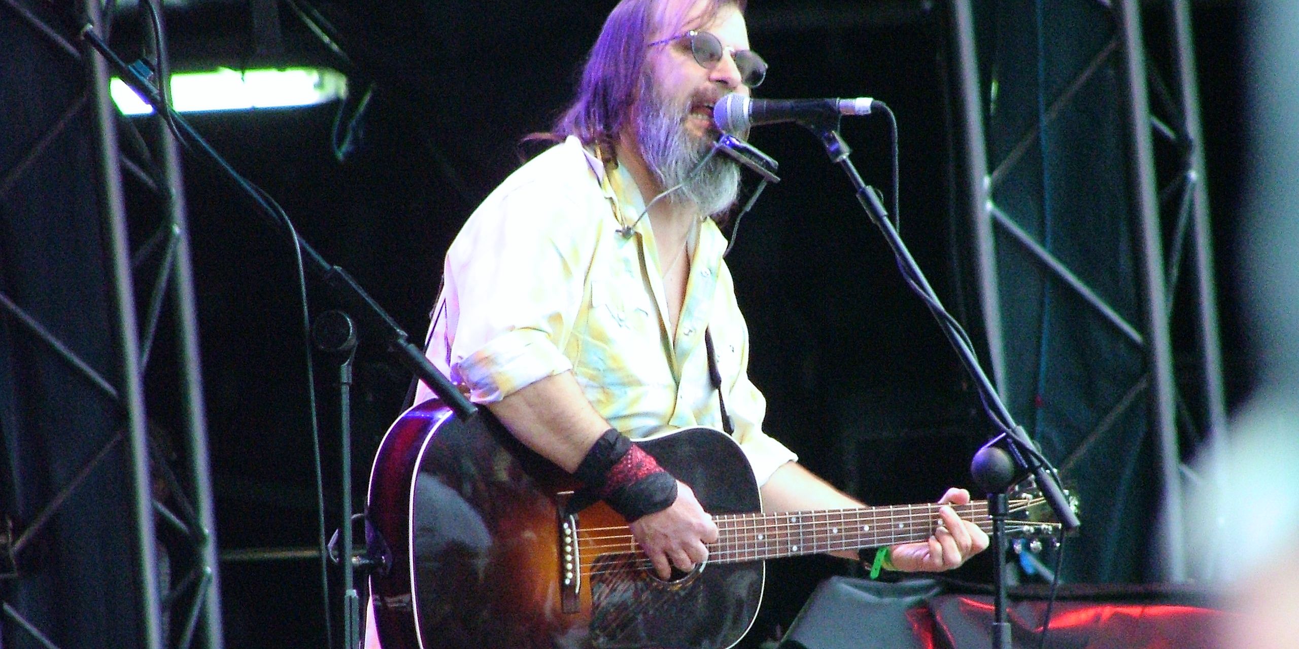 Steve Earle no palco Paling um violão e cantando em um microfone via Creative Commons