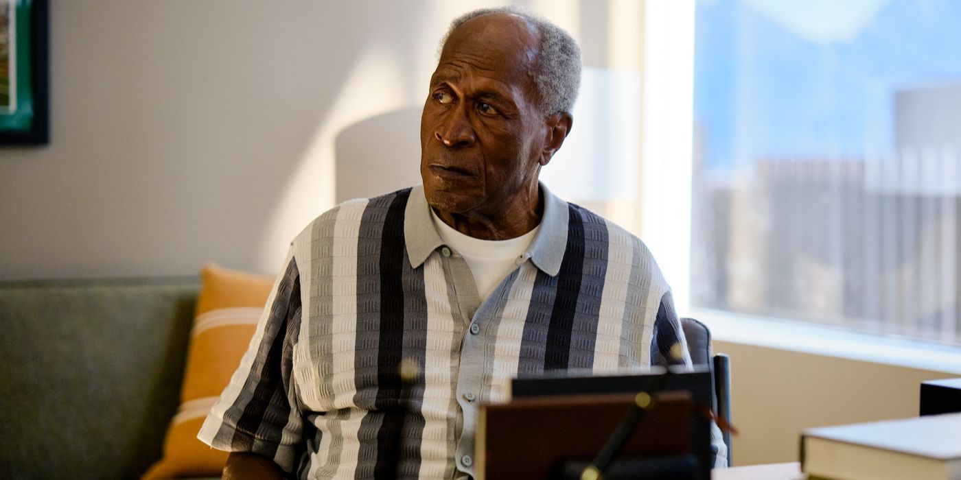 O ator John Amos sentado em uma camisa preta e branca na estreia da série LA